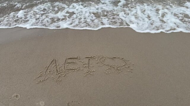 Cyrillic text leto written on wet sand with gentle sea foam nearby. Symbol of nostalgia and seasonal change from summer to autumn. Suitable for travel storytelling seasonal ads and memory themes.