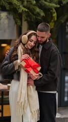 Obraz premium Young couple sharing a romantic moment with a Christmas gift outdoors in winter