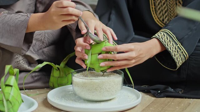 Two Muslimah brothers filling woven palm leaf pouches (Ketupat) with rice for Eid celebrations