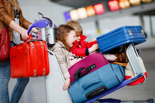 Two little kids, boy and girl, siblings and mother at the airport. Children, family traveling, going on vacation by plane and waiting on trolley with suitcases pushing by woman at terminal for flight.