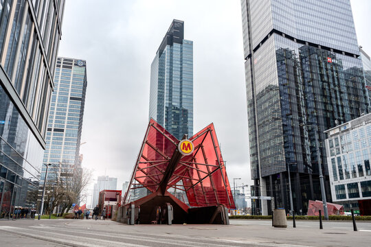 Entrance to a subway station with Warsaw Metro logo sign above, downtown city center skyscrapers visible in the background. Metro Warszawskie rapid transit system on March 24, 2025 in Warsaw, Poland.