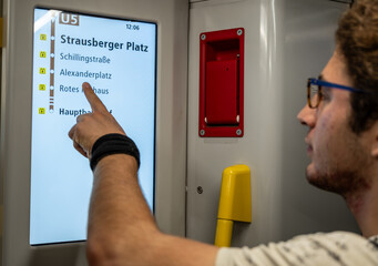 Berlin, germany, august 11, 2023. Young man tapping berlin u-bahn u5 digital route map at station, planning metro journey and checking connections on screen