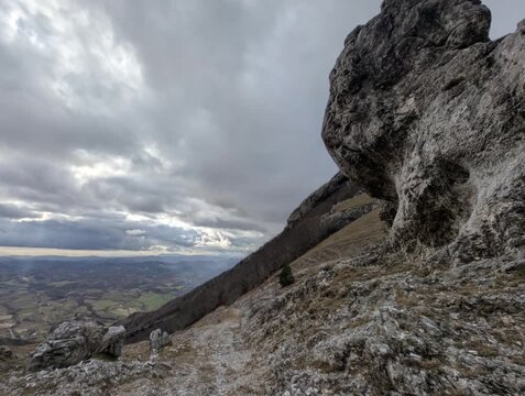 Paesaggio montano roccioso con grandi formazioni in primo piano, valle profonda e cielo nuvoloso 