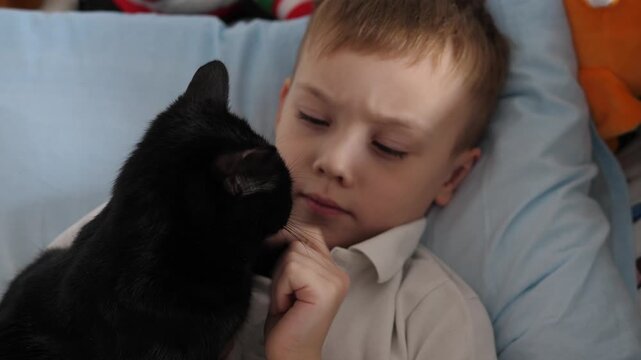 Happy little boy relaxing at home while cuddling his black cat. Warm, cozy family moment showing love, friendship and trust between child and pet.