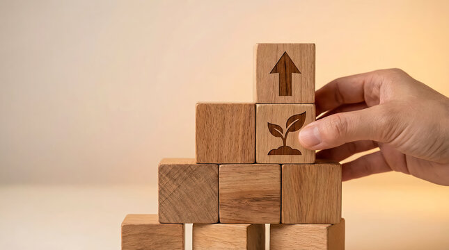 Hand placing wooden block with plant icon onto a growing stack of blocks symbolizing business growth, sustainability, investment, and career development