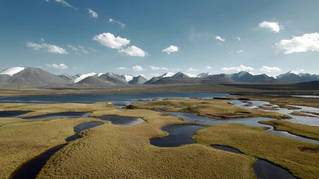 Drone footage over the other-worldly Arabel Plateau, featuring highland wetlands, shallow lakes, and distant snow-capped mountains in the remote landscape of Kyrgyzstan.