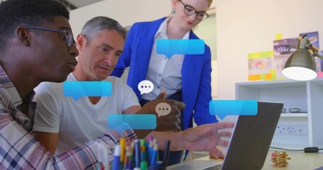 Working three-person team reviewing laptop with chat bubbles at office desk, woman in blue blazer