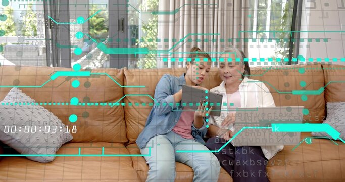 Pointing teen daughter in denim mom steadying tablet on living room couch teal overlay 00:00:03:18