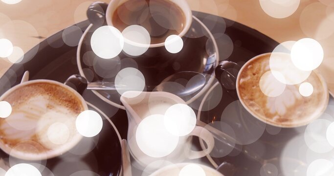 Displaying dark tray holding four coffee cups with latte art, milk jug, teaspoons on cafe table