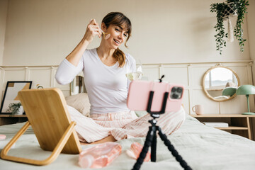 Woman recording a skin care tutorial with a facial roller and enjoying self-care