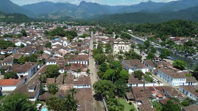 Drone flight parallel to Rio Pereque Acu in Paraty, Brazil, passing over Rua Marechal Deodoro. Features Nossa Senhora dos Remedios church, mountains, and Atlantic forest in the background.