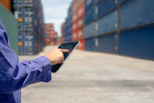 Logistics worker using tablet at container yard, checking shipping containers and inventory outdoors, showing modern logistics, supply chain control and industrial work.