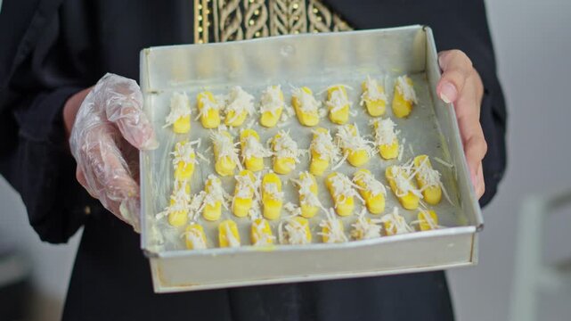 Woman in black kaftan holding tray of raw Kaasstengels cheese cookies
