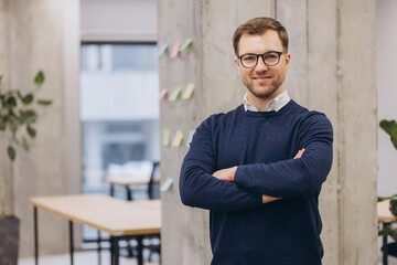 Obraz premium Smiling professional man with glasses standing confidently in a modern office space, showcasing a productive and welcoming work environment