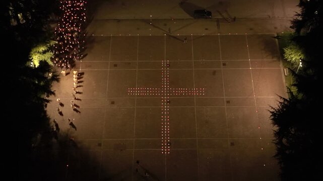 Aerial view of worshippers carrying candles around a large cross formed with lights during the Candlemas celebration at Santa Barbara Church in Italy.