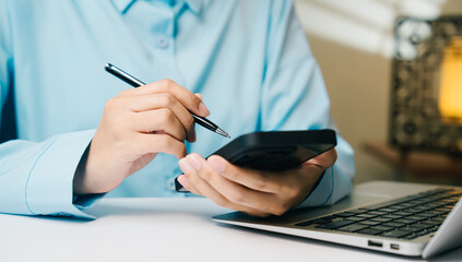 Fototapeta premium Person using calculator with pen near laptop on white desk, focused on financial calculation and work in office environment