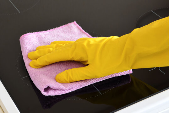 Hand in Yellow Glove Cleaning a Black Induction Stovetop close up