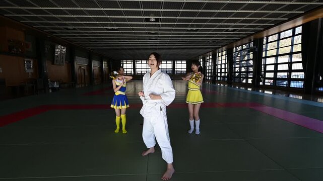 道場で空手の型を決める母親を応援するチアリーダー姿の子供たち