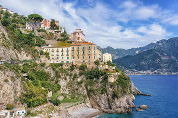 Naklejka premium Amalfi Coast, Italy. Coastal view of colorful buildings perched on a cliffside overlooking the Mediterranean Sea with mountains in the background under a clear blue sky