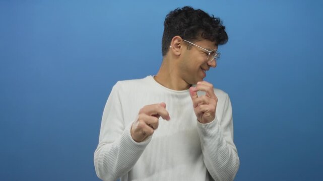 Man with clenched fists and eyeglasses standing in a studio setting against a vibrant blue backdrop; disgust.
