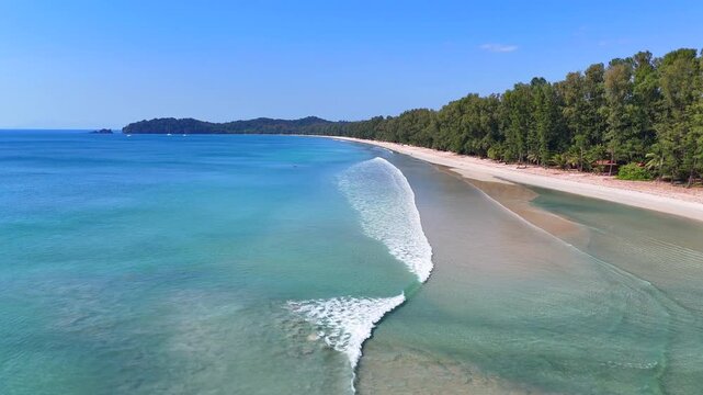 Aerial view of Koh Phayam beach, gentle waves, tropical trees, and calm turquoise sea on a sunny day.