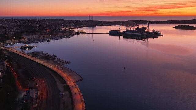 Aerial view of cranes in the harbor reflecting the sunset colors contrasting with the dark water, Pula, Istria County, Croatia.