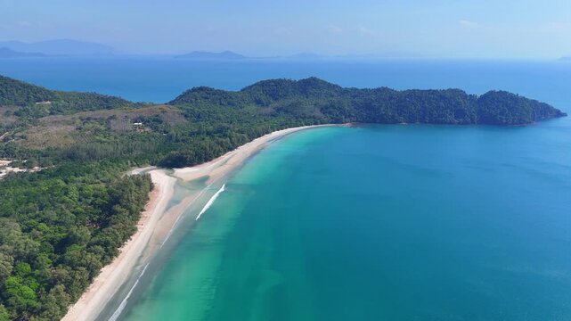 Aerial view of Koh Phayam coastline revealing turquoise bay, sandy beach, forested hills, and calm tropical sea under clear skies.