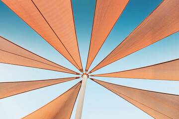 Multiple triangular shade sails connected to a central pole, forming a star like composition against a bright blue expanse