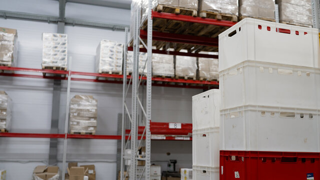 Stacking plastic crates in a modern industrial warehouse with high shelving racks holding palletized goods