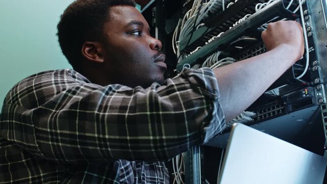 Young man works with server rack and network cables in a data center during daytime hours