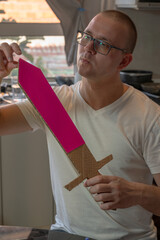 Man crafting a cardboard sword at a table using cardboard, colored paper, and glue. DIY handmade project concept, creativity, imagination, hobby, and eco-friendly low-budget craft.