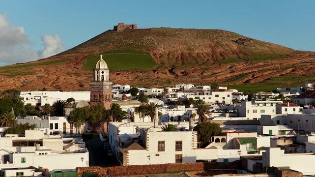 Aerial view of the white-washed buildings of Teguise, highlighted by the church tower and the contrasting colors of the volcanic mountain, Teguise, Canary Islands, Spain.