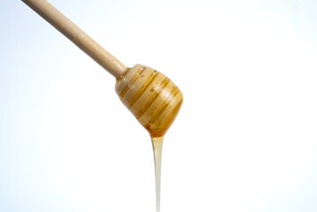 Wooden honey dipper with flowing honey isolated on white background. Minimal food photography, natural sweetness and organic product concept. 