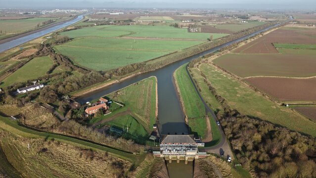 Aerial view of the Hobhole Pumping Station where a canal splits into two, lined with manicured green grass and trees, Hobhole, Boston, United Kingdom.