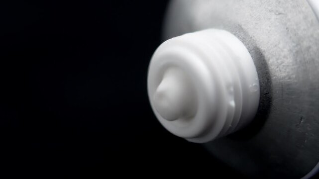 White cosmetic cream being squeezed from a tube on a black background. Macro shot