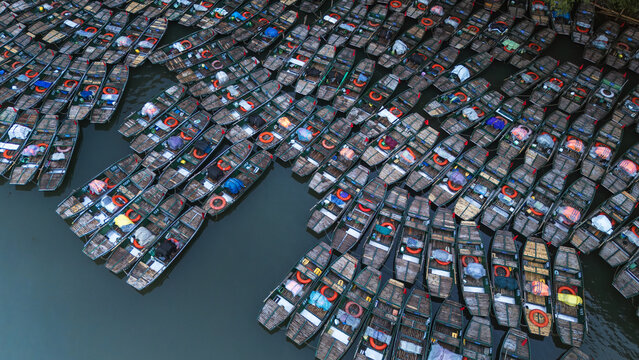 Aerial view of a multitude of boats clustered tightly together on the water, their dark hulls contrasting with the colorful contents, Ninh Nhat, Ninh Binh, Vietnam.