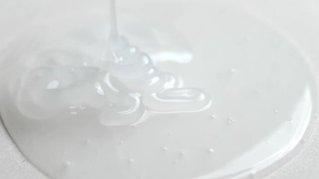 White liquid soap pouring in slow motion forming smooth glossy waves and bubbles on the surface. Close up hygiene and skincare product texture