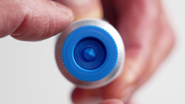 A hand with dehydrated skin opening a tube of medicated moisturizing cream on white background. Dermatological treatment concept