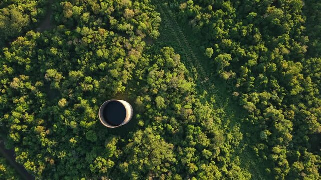 Aerial of industrial power plant infrastructure embedded within dense green forest, smokestack and cables to grid converters