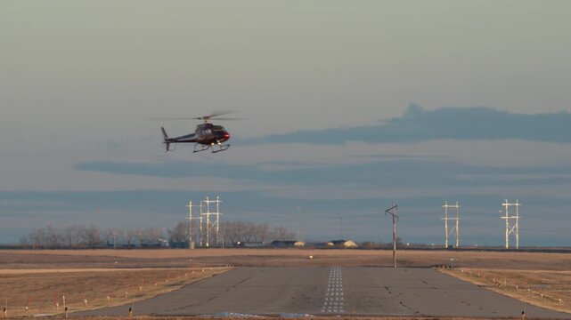 A small helicopter crosses over a runway to land at a small airport