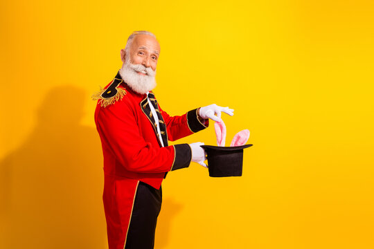 Elderly magician in red circus costume performs bunny trick against bright yellow background during holiday show
