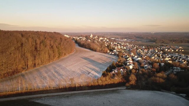 Forward-moving drone flight over frosty agricultural fields toward Elchingen, with forest edge on the left and a clear winter sky over the distant village and valley.