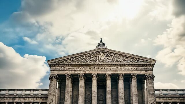 The large building features classical columns and intricate carvings. The sky is partly cloudy, adding atmosphere to the structure and its surroundings.