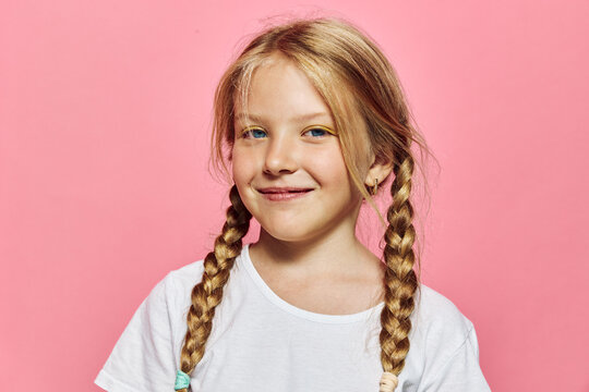 Smiling young girl with blonde braided hair and white shirt posing on a pink background studio portrait.