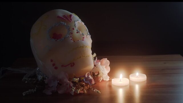 Atmospheric video featuring a decorative skull inspired by Day of the Dead, placed on a wooden table with glowing candles and floral elements.