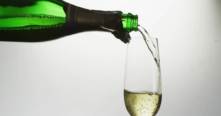 Pouring green bottle with torn foil sending golden stream into tall flute at studio with bubbles