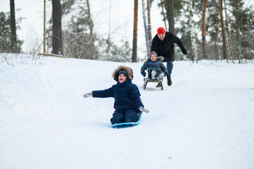 Father and young children sledding down snowy hill in winter forest. Seasonal family leisure, childhood fun, and active lifestyle in cold weather nature