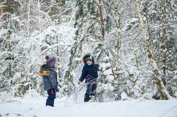 Two young children enjoying active winter day outdoors in snowy forest. Kids play, explore nature, ride a sled, and have fun among snow-covered trees.
