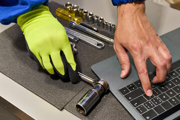 High-angle shot of an unrecognizable repairman's hands grabbing a tool from his toolbox and consulting his laptop for information about the car.