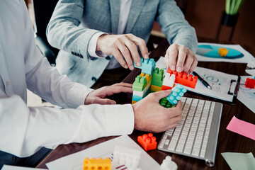 Two colleagues collaborate at a busy office desk using colorful building blocks and a keyboard to plan and innovate together © deagreez